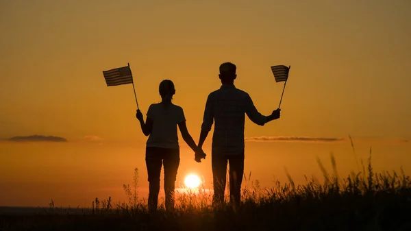 Junges Paar mit US-Flaggen an einem malerischen Ort bei Sonnenuntergang — Stockfoto