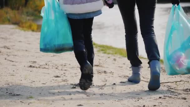 Mulher voluntária com uma criança caminhar ao longo do lago, transportar pacotes com lixo. Vista traseira — Vídeo de Stock