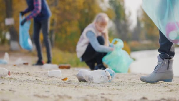Egy csapat önkéntes szemetet szed fel a tónál, műanyag hulladékot pakol zsákokba. — Stock videók