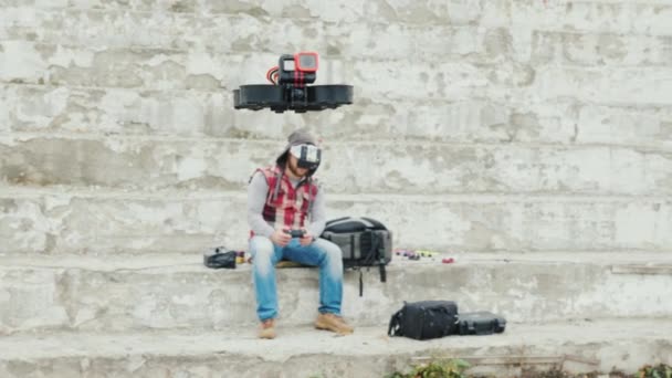 A man in a helmet with telemetry controls a drone that flies in front of him — Stock Video