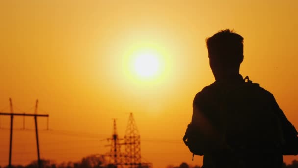 Un hombre con una mochila detrás de él está de pie sobre el fondo del paisaje urbano en la distancia y la puesta de sol . — Vídeos de Stock