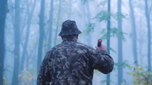 En man med ficklampa i handen går genom skogen i dimman. Söker i skogen — Stockvideo