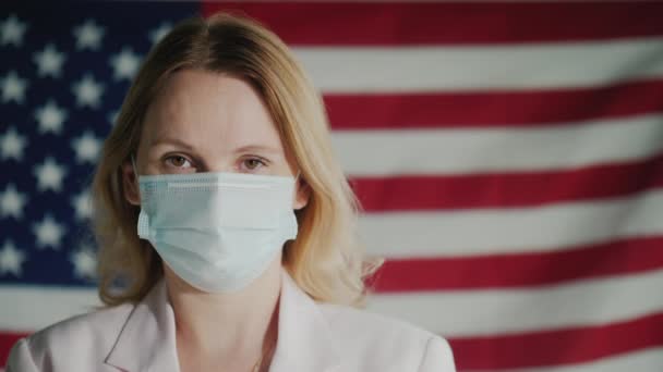 Retrato de una mujer de un hombre de negocios con una máscara protectora en el fondo de la bandera de Estados Unidos — Vídeo de stock