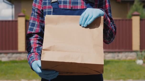 Ein Kurier in Handschuhen hält eine Tüte mit Lebensmitteln in der Hand. Hauszustellung — Stockvideo
