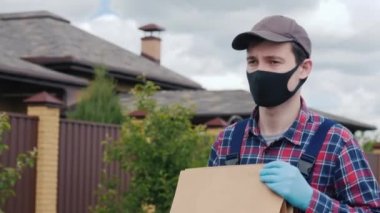 Maske ve eldiven takan bir adam alışveriş torbalarını müşterilerin evine taşır.