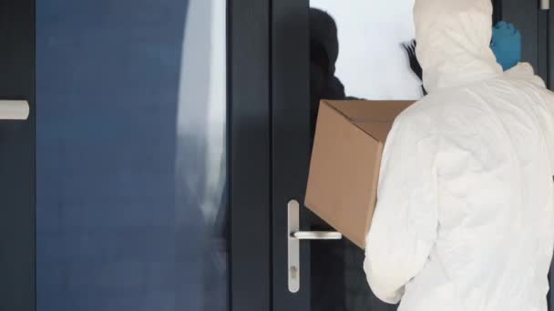 Чоловік у захисному костюмі приніс коробку до дверей — стокове відео