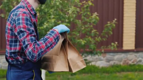Vue latérale : Un homme portant un masque et des gants transporte des sacs d'épicerie à la maison des clients — Video
