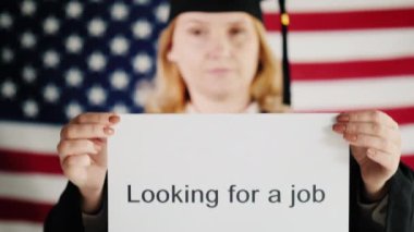Manto ve şapkalı bir mezun iş arama hakkında bir poster tutuyor. ABD 'de istihdam