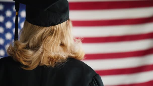 Graduado con un diploma en el fondo de la bandera de Estados Unidos. Vista desde atrás — Vídeo de stock