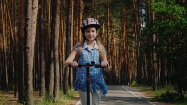 Радостный ребенок ездит на электрическом скутере по дороге в парк — стоковое видео