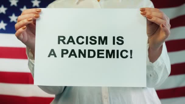 Γυναίκα κατέχει αφίσα Ρατσισμός είναι πανδημία σε αμερικανική σημαία φόντο. Διαδήλωση για τα ανθρώπινα δικαιώματα — Αρχείο Βίντεο