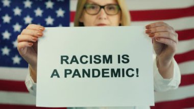 Amerikan bayrağı geçmişinde ırkçılığın salgın olduğu posterini tutan genç bir kadın. İnsan Hakları Gösterisi