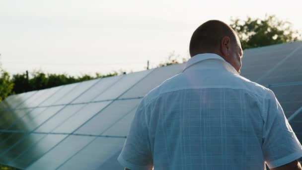 Vista trasera: El propietario de la planta de energía doméstica camina a lo largo de la fila de paneles solares — Vídeos de Stock