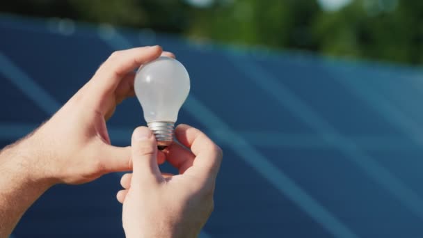 Руки каменщиков держат лампочку на фоне солнечных панелей — стоковое видео