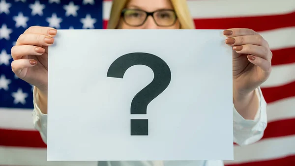 Eine Frau hält ein Plakat mit einem Fragezeichen vor dem Hintergrund der amerikanischen Flagge — Stockfoto