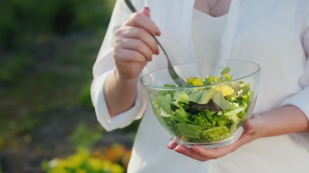 Een vrouw eet salade, staat bij het bed waar het groeit. — Stockvideo