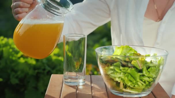 Un desayuno saludable cerca de su pequeño huerto. Una mujer vierte jugo en un vaso — Vídeos de Stock