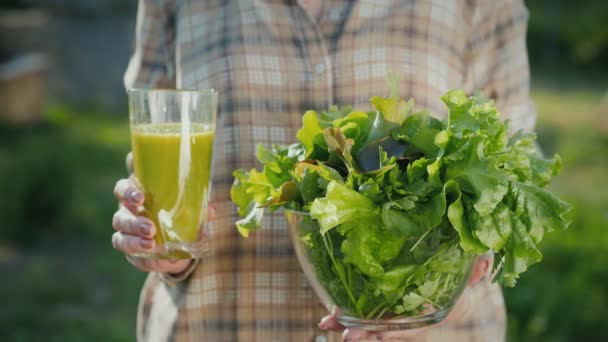 Uma mulher segura um copo de smoothie verde e um prato de alface. Alimentação saudável e dieta — Vídeo de Stock