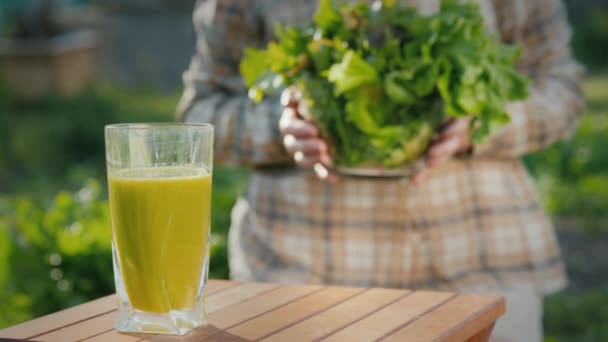 Een vrouw doet een bord sla bladeren rond een glas groene smoothie. Vitaminedrank — Stockvideo