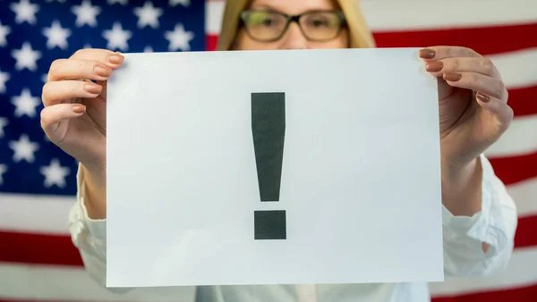 Vrouw houdt een poster met een uitroepteken tegen de achtergrond van de Amerikaanse vlag — Stockfoto