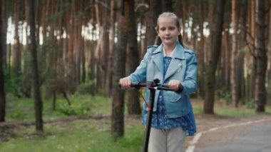 Yan görüş: neşeli çocuk parkta yolda elektrikli scooter kullanıyor
