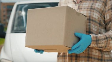 Bir teslimat işçisi bir paket tutuyor, bir minibüsün yanında duruyor.