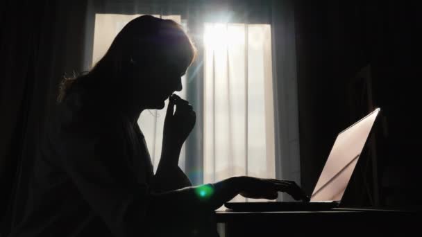 Silueta de una mujer junto a la ventana, hablando con auriculares, trabajando en el concepto de casa — Vídeos de Stock