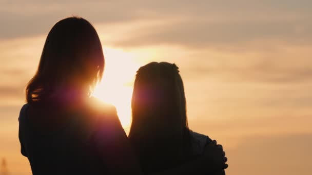 Uma mulher gentilmente abraça sua filha, observando o pôr do sol juntos — Vídeo de Stock