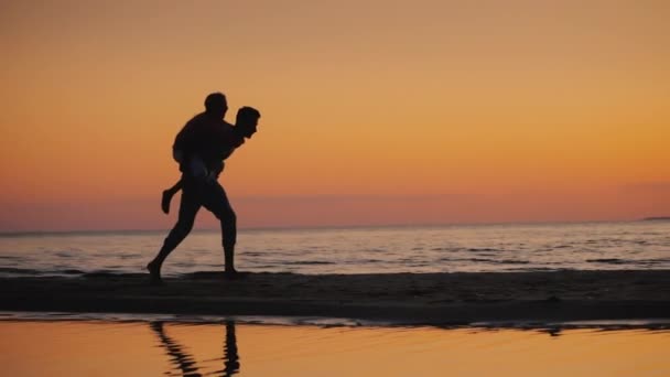 Hermano juega con su hermana menor en la playa - la enrolla sobre sus hombros — Vídeos de Stock