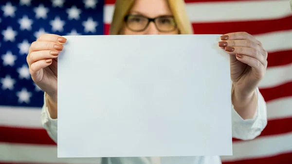 Frau hält ein leeres Plakat, steht vor dem Hintergrund der amerikanischen Flagge — Stockfoto
