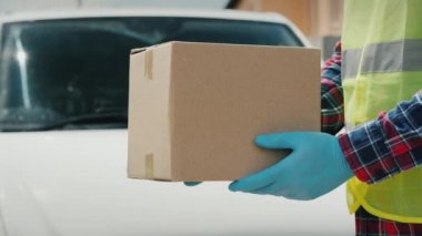 Üniformalı bir ulak beyaz bir minibüsün arka planında bir paket tutuyor.