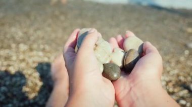 Sahilde otururken bir avuç dolusu çakıl taşı tutan bir adam.