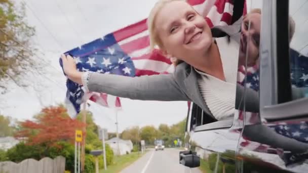 Una donna con una bandiera americana guarda fuori dal finestrino di un'auto in movimento. Travel America Concept. Video al rallentatore — Video Stock