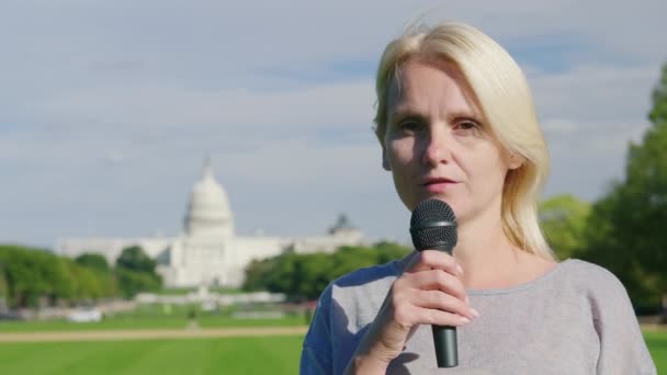 En ung kvinnlig reporter berättar nyheten i en mikrofon mot bakgrund av Capitol Building i Washington, DC — Stockvideo