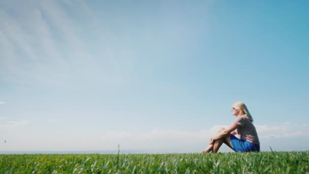 Vista laterale della donna che si gode le vacanze estive, seduta sull'erba verde, vista posteriore — Video Stock