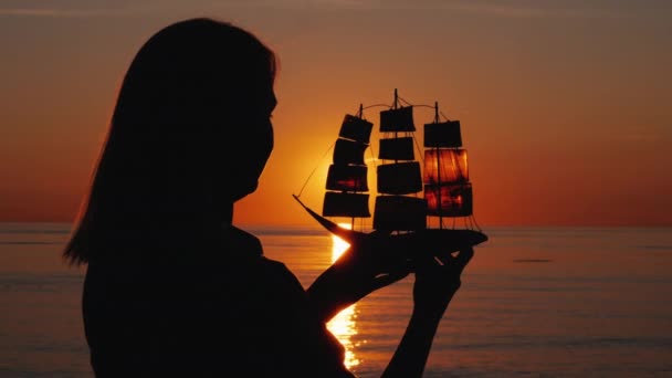 Silhuett av en kvinna med en segelbåt i händerna, den nedgående solen skiner genom seglen. Inspiration koncept — Stockvideo