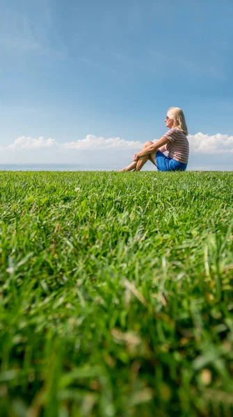 Junge Frau sitzt im Gras an einem malerischen Ort, idyllische Sommerlandschaft — Stockfoto