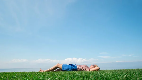 Μια γυναίκα είναι ξαπλωμένη στο πράσινο γρασίδι, πίσω της μπορείτε να δείτε τη λίμνη Οντάριο.. — Φωτογραφία Αρχείου
