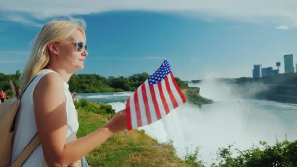 Vista lateral da mulher com a bandeira da América em sua mão admira Niagara Falls — Vídeo de Stock