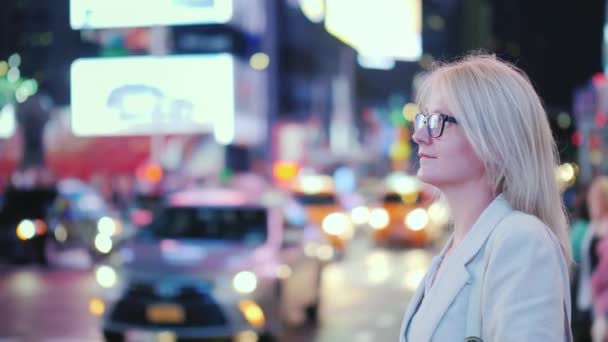 Uma mulher está em Times Square em Nova York, táxis amarelos reconhecíveis estão passando por um símbolo da cidade — Vídeo de Stock