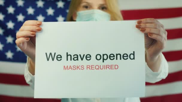 A woman holds a poster informing about opening a business after quarantine. Against the backdrop of the American flag — Stock Video