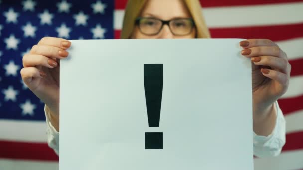 Egy nő egy felkiáltójellel ellátott posztert tart az amerikai zászló hátterében. — Stock videók