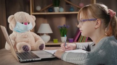 İnternette okul var. Öğrenci laptopun yanında koruyucu maskeli bir ayının yanında ders yapıyor.