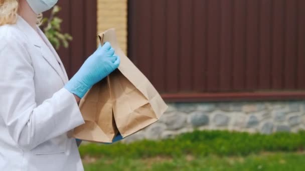 Vista lateral: Una mujer con una máscara y guantes lleva bolsas de comida a su casa — Vídeos de Stock