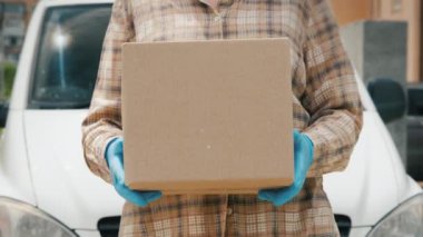 Elinde karton kutu olan kurye teslimat minibüsünün arka planında duruyor.