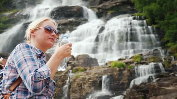 Mujer feliz bebe agua clara de una cascada en Noruega — Vídeos de Stock