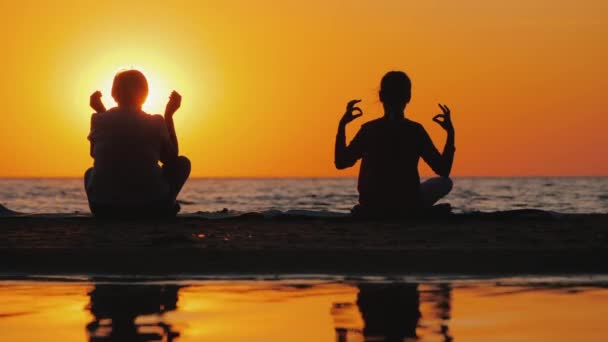 Two women meditate on the beach at sunset — Stock Video