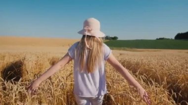 Şapkalı bir çocuk buğdaylı yolda yürüyor, yazın ve güzel havanın tadını çıkarıyor.