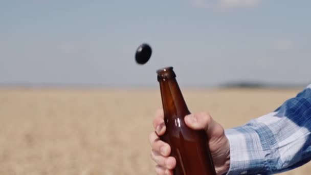 Man opens a bottle of beer against the backdrop of a wheat field. Slow motion video — Stock Video
