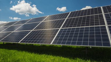 Güneş panelleri mavi gökyüzüne karşı Bulutlar ve altında yeşil çimenler